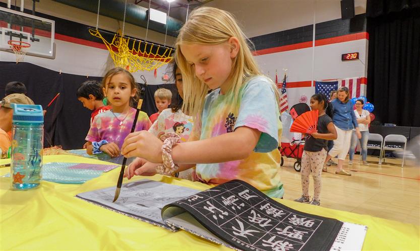 A girl attempts to write using a paintbrush during International Day
